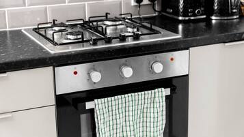 A kitchen with a gas stove, oven, and a hanging green and white checkered towel.