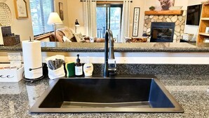 A kitchen with a granite countertop, a black sink, and a stone fireplace.