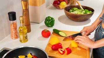 A kitchen counter with various vegetables being chopped, a cutting board, a bowl of salad, and a bottle of oil.