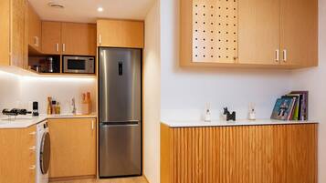 Eine kleine Küche mit Holzschränken, einem Edelstahlkühlschrank, einer Mikrowelle und einer Waschmaschine.