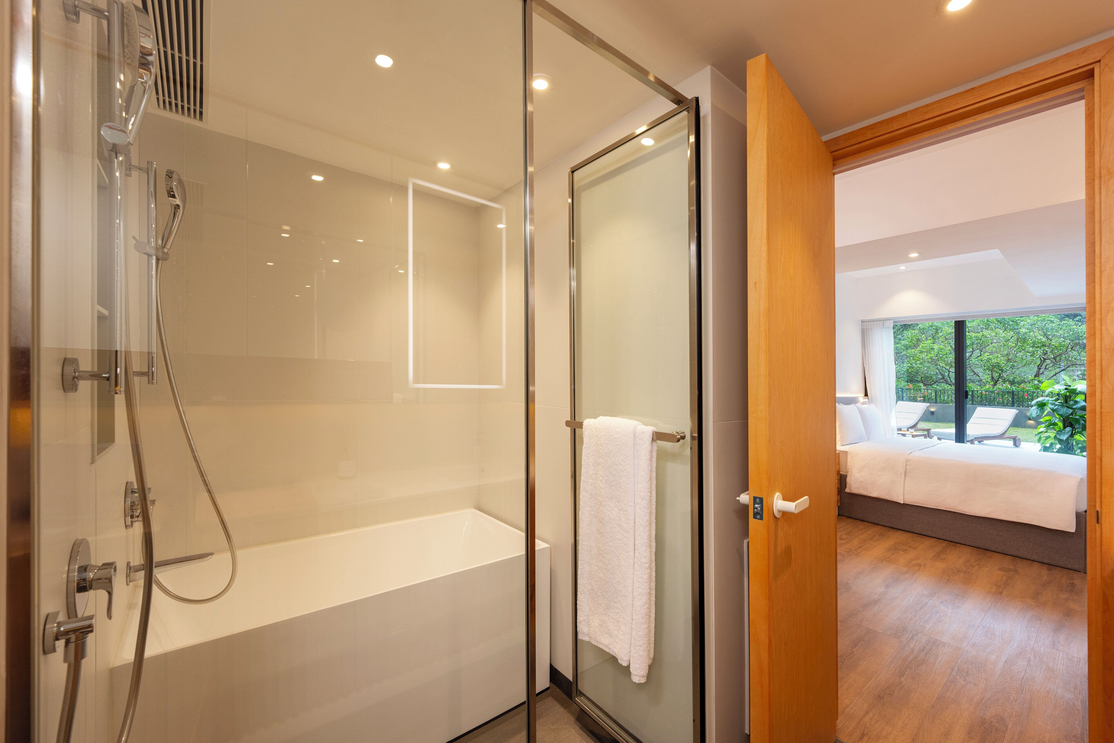 Ein modernes Badezimmer mit einer Glaskabine zur Dusche, einer weißen Badewanne und einem Handtuch an einem Halter.
