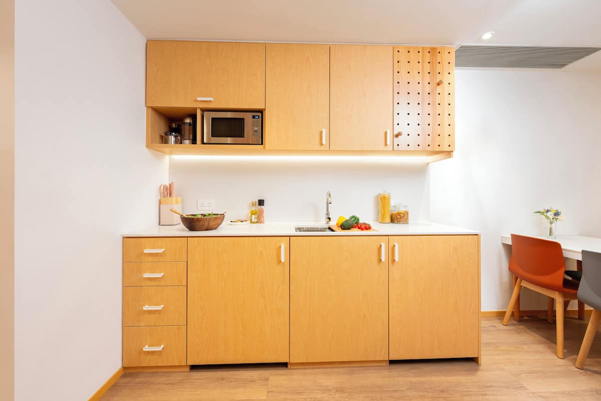 Een moderne keuken met houten kastjes, een magnetron en een eethoek met een tafel en stoelen.