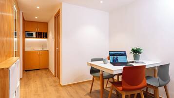 A compact kitchen with wooden cabinets and a microwave, a dining area with a white table and two chairs, and a laptop on the table.