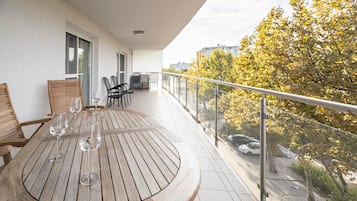 A round wooden table with chairs and wine glasses on a balcony with a glass railing.