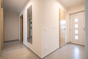 A hallway with a door on the right, a mirror on the left, and a light switch on the wall. - LB - Garden Pearl II Siófok (Siófok)
