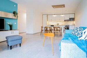 A modern living room with a sofa, ottoman, and a dining area with chairs and a table.