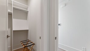 Ein begehbarer Kleiderschrank mit geöffneten Türen, ein Holzstuhl und eine weiße Wand mit Steckdose.