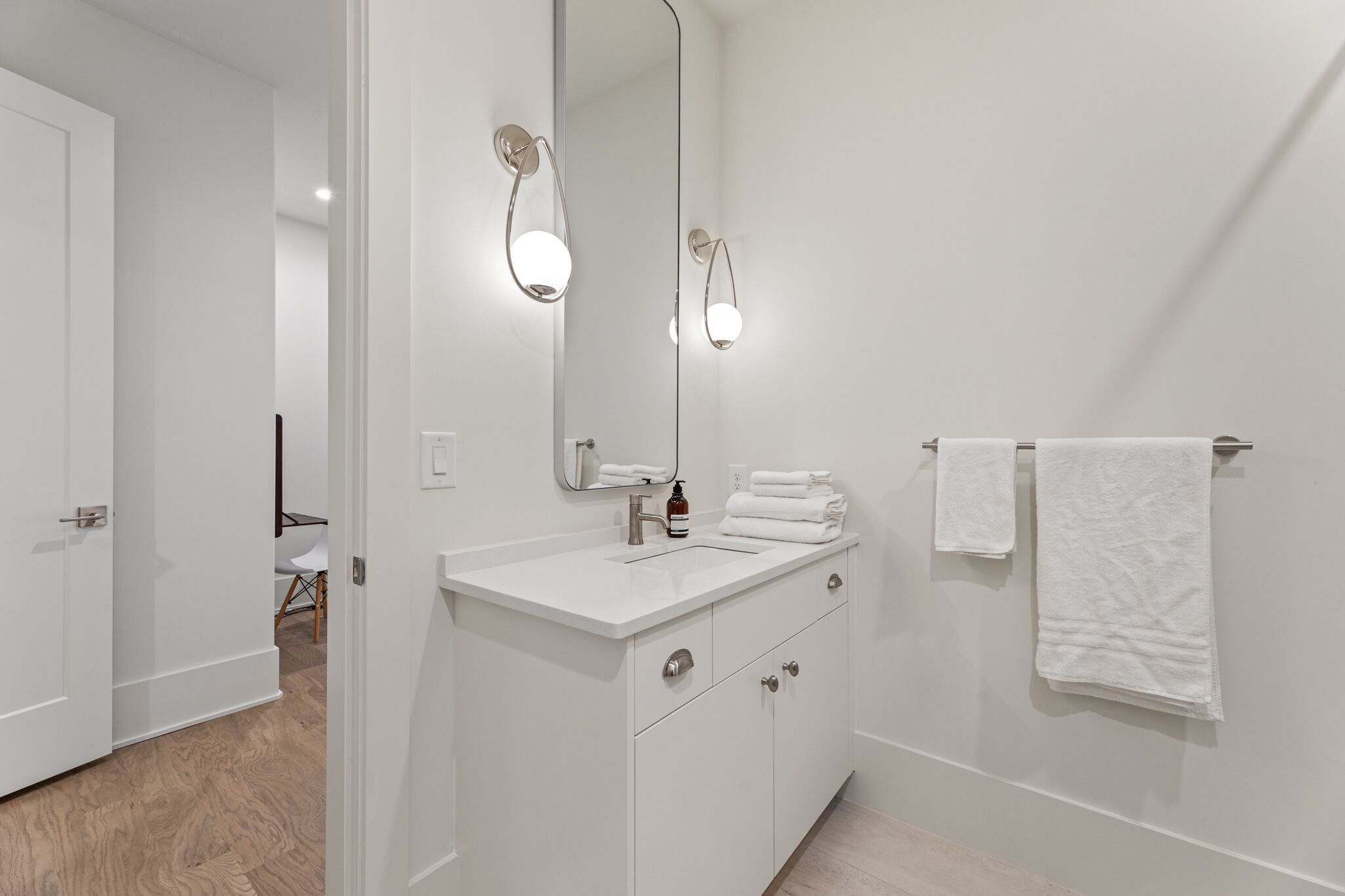 Un baño moderno con tocador blanco, un espejo grande y dos luces empotradas.