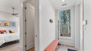 Ein modernes Schlafzimmer mit einem Bett, einer Bank und einem großen Fenster mit Blick auf Bäume.