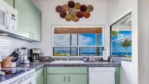 Een keuken met groene kastjes, een witte vaatwasser, een koffiezetapparaat en een raam met uitzicht op palmbomen.