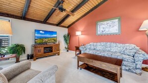 A living room with a wooden ceiling, a large flat-screen TV, a floral sofa, and a wooden coffee table. - Wailea Ekolu, #312 1 Bedroom Condo by RedAwning (Kihei)