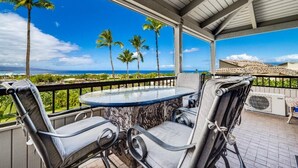 A covered outdoor seating area with a table and chairs, overlooking a landscape with palm trees and a view of the ocean. - Wailea Ekolu, #312 1 Bedroom Condo by RedAwning (Kihei)