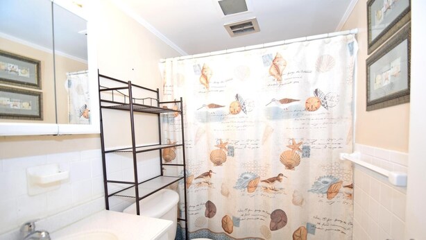 Une salle de bain équipée de toilettes, d’un lavabo et d’un rideau de douche orné d’un motif représentant des oiseaux et des coquillages.