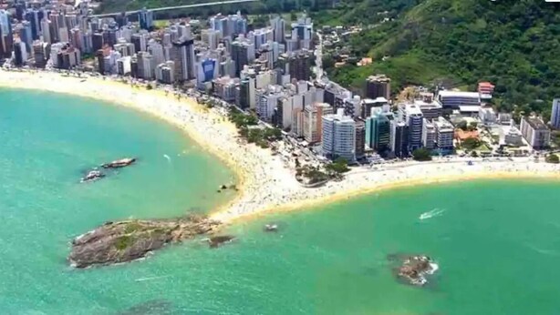 Vista aérea de una ciudad costera con rascacielos, una playa de arena y aguas turquesas cristalinas.