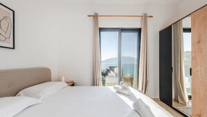 A modern hotel room with a large bed, a view of the sea, and a wooden door.