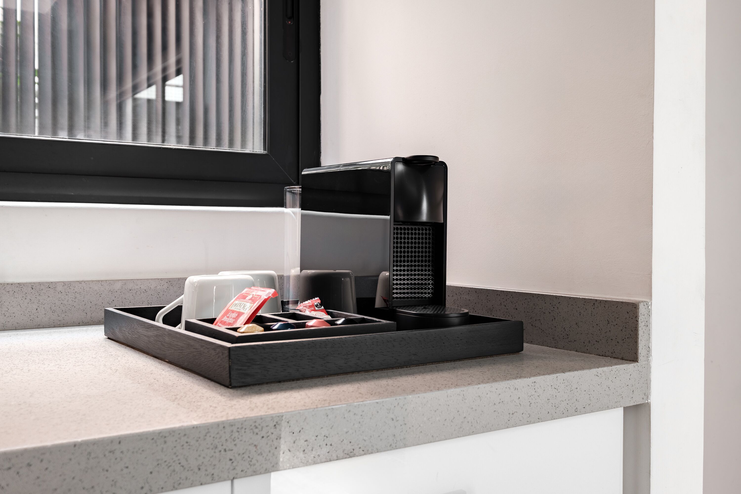 Un comptoir de cuisine avec une machine à café, un verre et un plateau contenant des ustensiles et un sachet de sucre.