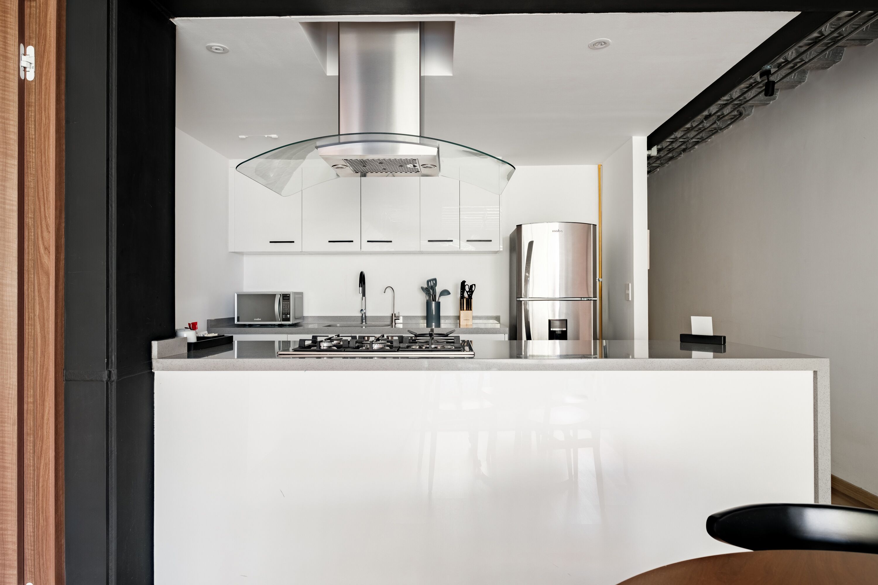 A modern kitchen with a central island, stainless steel appliances, and a glass hood over the stove.