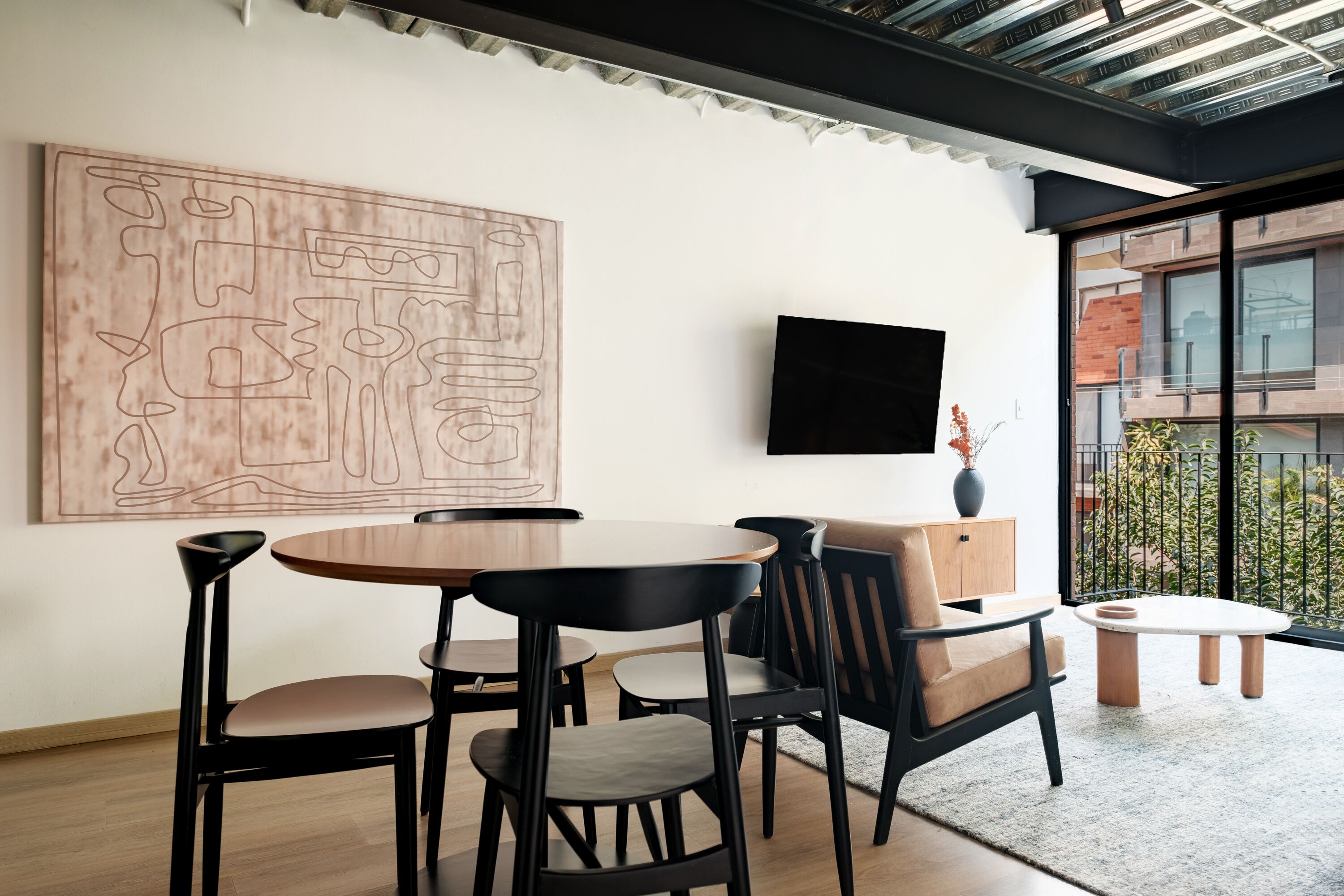 A modern dining area with a round table, black chairs, and a large abstract painting on the wall.