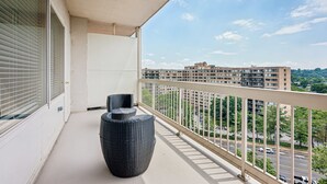 Een balkon met uitzicht op een stadslandschap, met een grote rieten stoel en een bijzettafeltje.