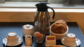 Una bandeja para el desayuno con café, leche, huevos, pan y pastelería, junto a una ventana que ofrece vistas a una escalera y plantas en macetas.