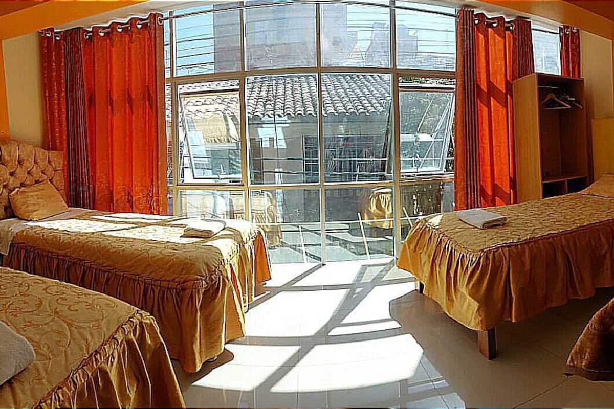 Une chambre d’hôtel avec deux lits, une grande fenêtre avec des rideaux, une armoire et une lampe.