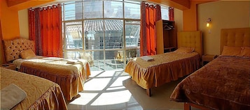 Quarto de hotel com duas camas, uma janela grande com cortinas, um guarda-roupa e uma luminária.