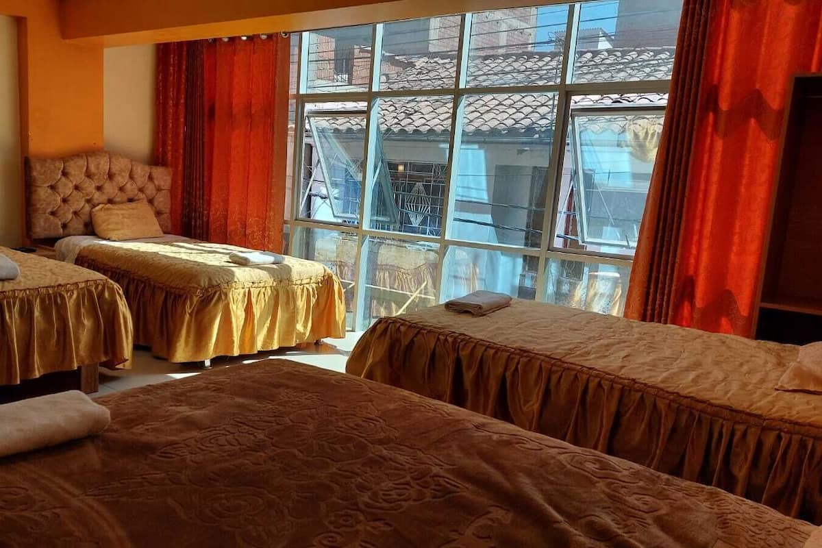 Une chambre d’hôtel avec deux lits, une grande fenêtre avec des rideaux rouges et une vue sur les bâtiments environnants.