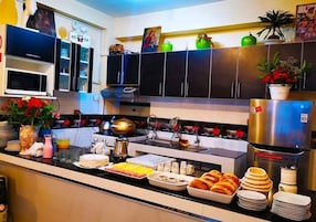 Cozinha com sistema de buffet, incluindo frigorífico, micro-ondas, pia e diversos alimentos.