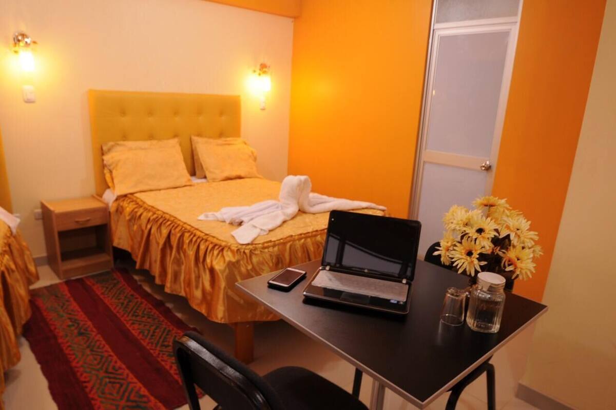 Une chambre d’hôtel avec un lit, une table de chevet, un ordinateur portable et un vase de fleurs.