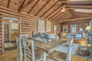 A log cabin interior with a wooden dining table, white chairs, a sofa, and a fireplace. - Cowboy Cabin (Cascade)