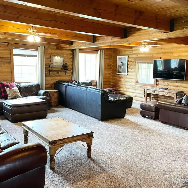 Ein rustikales Blockhaus-Interieur mit einer großen Couch, einem Couchtisch und einem Fernseher.
