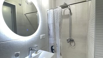 Een badkamer met een witte wastafel, een spiegel, een douche met glazen deur en een plafondlamp.