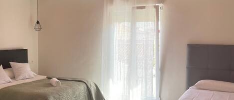 A hotel room with two beds, a large window with sheer curtains, a marble floor, and a hanging light fixture.