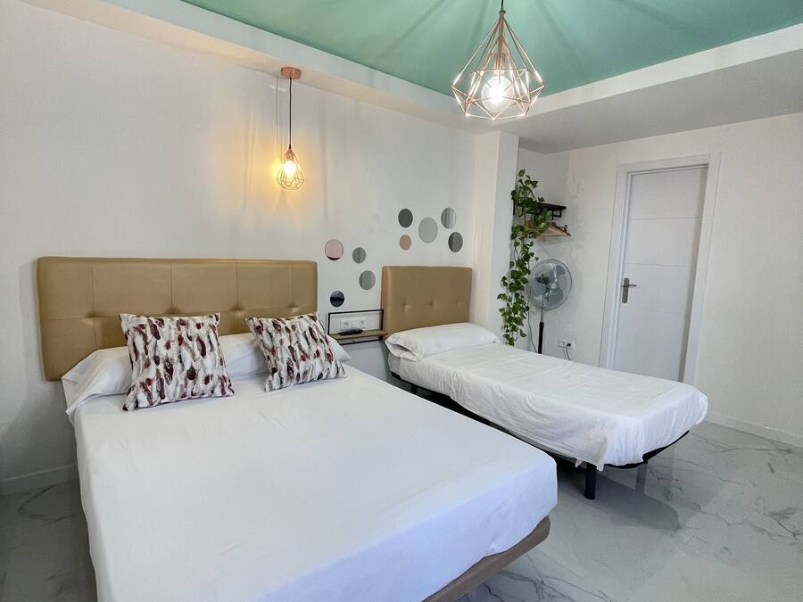 A hotel room with a large bed, a smaller bed, a ceiling fan, and a wall-mounted light fixture.