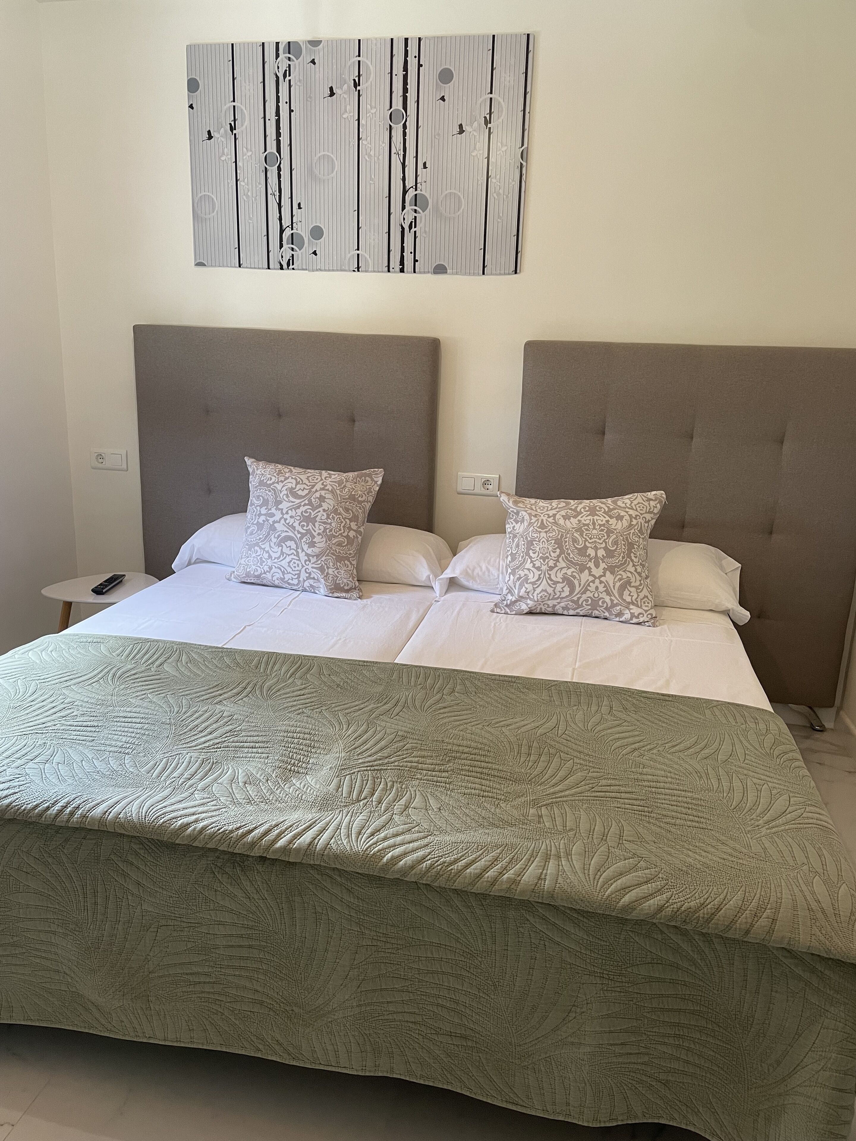 A double bed with a leaf-patterned bedspread, two matching pillows, and a wall-mounted abstract art piece above.