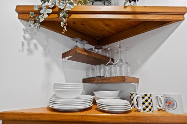 A wooden shelf with glassware and white plates.