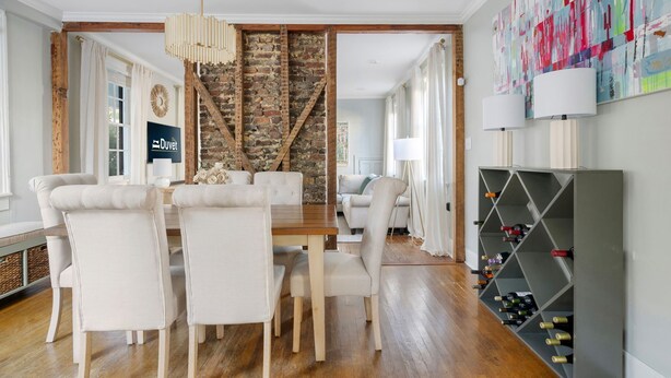 A dining area with a wooden table and chairs, a brick wall, and a wine rack. - Backyard Serenity, Balcony Views | Palmetto House (Charleston)