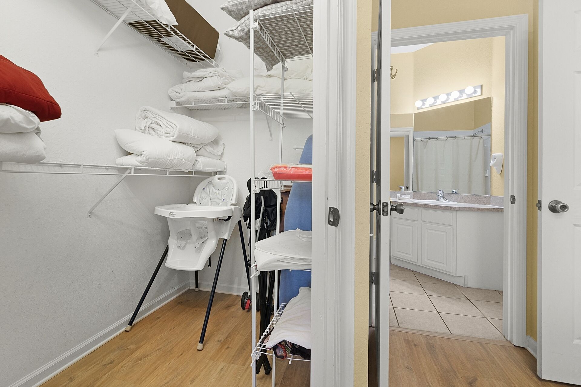 Un lavadero compacto y bien organizado, con estantes para colgar ropa, un espacio pequeño para planchar y una puerta que da a un baño con espejo e iluminación.