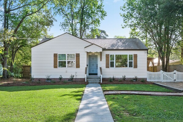 A single-story house with a front door, a small porch, and a white picket fence.