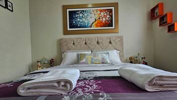 Een net opgemaakt bed met opgevouwen handdoeken, een decoratief kussen en een kleurrijk schilderij erboven.