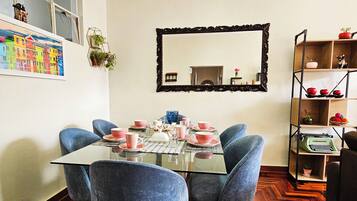 Een eetkamer met een glazen tafel, blauwe stoelen en roze servies.