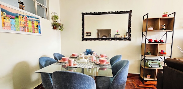 A dining room with a glass table, blue chairs, and pink dishes.