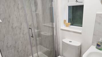 Une salle de bain moderne avec une douche à parois de verre, des toilettes, un lavabo et une petite fenêtre.