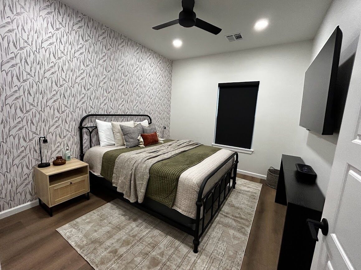 A bedroom with a bed, bedside table, lamp, and a ceiling fan.