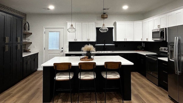 A modern kitchen with a large island, dark cabinets, stainless steel appliances, and pendant lighting.