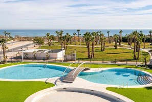 Una piscina con un puente, rodeada de palmeras y vista al océano.