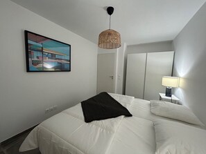 A bedroom with a bed, a hanging light fixture, a bedside table with a lamp, and a painting on the wall. - Jardin Secret C01  by Avecoeur (Antibes)