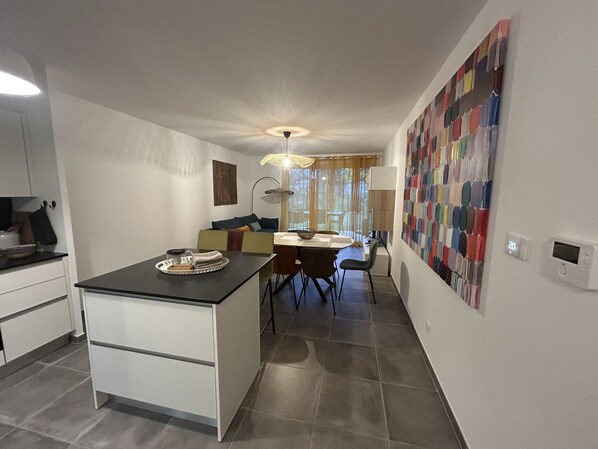 A compact kitchen with a dining area, a small island, and a colorful abstract wall art. - Jardin Secret C01  by Avecoeur (Antibes)