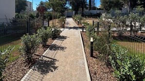 A pathway lined with trees and shrubs, leading towards a building with a white facade.