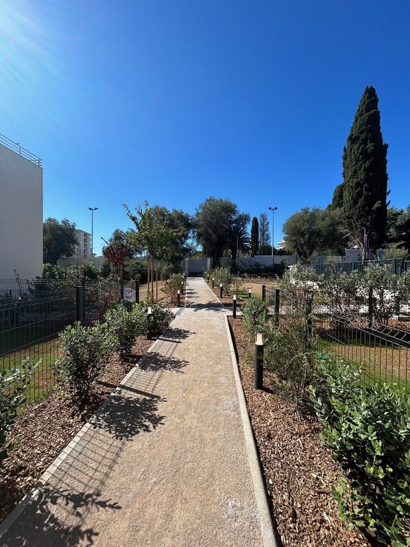 Un sendero bordeado de árboles y arbustos que conduce a un edificio de fachada blanca.